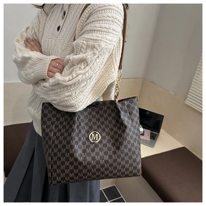 Detail of coffee tote bag with M-pattern print, chain strap, and golden logo emblem