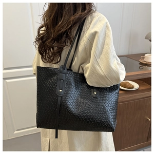 Detail of a black woven tote bag with metallic studs worn by a model in a cozy cafe setting