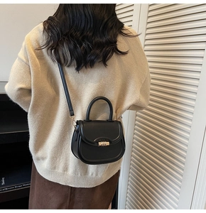Modèle portant un sac selle noir avec fermoir doré sur une jupe brune et un pull beige