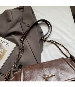 Detail van donkerbruine leren handtas met gouden hardware en kettingriem op een blazer