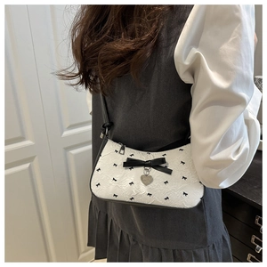 Gros plan du sac baguette blanc avec nœuds noirs et pendentif cœur en argent brillant