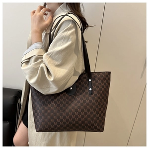 Detail of large brown tote bag with M-letter print shown on shoulder with light trench coat