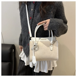 Sac à bandoulière chic en daim beige avec détails dorés porté par un mannequin
