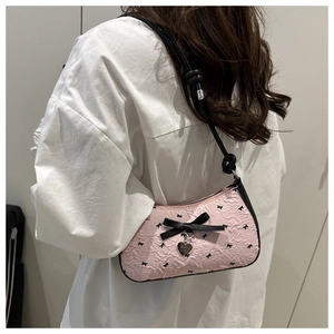 Pink bow shoulder bag with pleated texture and silver heart pendant on a model