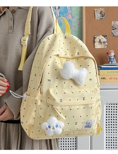 Détail d'un sac à dos jaune à pois avec breloques en peluche et nœud dans un décor école