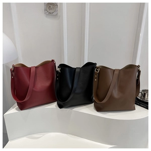 Trois sacs seaux en cuir bordeaux, noir et marron sur un présentoir de style minimaliste