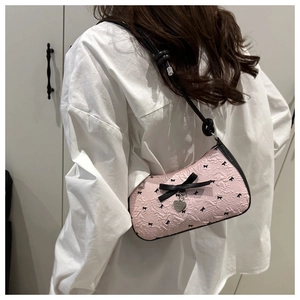 Détail du sac sous le bras rose gaufré avec nœud noir et breloque en forme de cœur