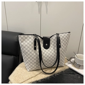 Macro detail of tote bag showing M-letter print pattern and black leather buckle strap