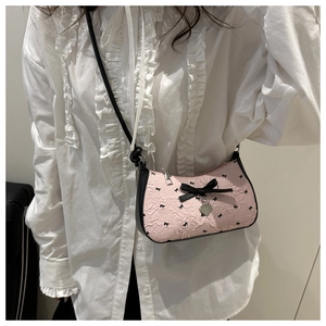 Détail du sac rose à nœuds avec pendentif cœur argenté sur une chemise à volants
