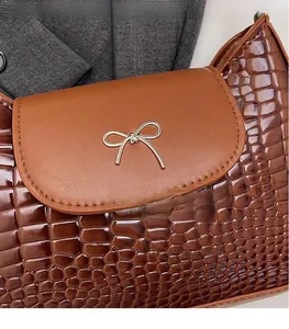 Détail d'un sac en cuir marron foncé à motif crocodile avec nœud doré métallique