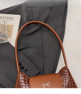 Détail d'un sac porté épaule marron texture crocodile avec nœud métallique et bandoulière