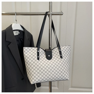 Detail view of large tote bag with M-letter print, black straps, and metal rivet accents