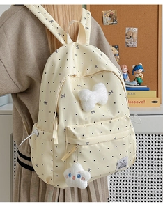 Détail d'un sac à dos crème à pois avec nœud en peluche et pendentif étoile en situation