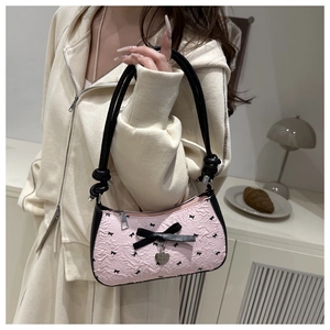 Sac à bandoulière rose à motifs nœuds porté par un mannequin dans un décor chaleureux