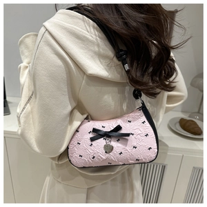 Détail du sac sous l'aisselle en jacquard rose avec imprimé nœud noir et breloque cœur porté