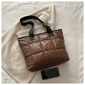 Vue à plat d'un sac cabas matelassé marron sur un blazer beige avec des anses noires