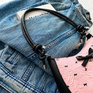 Detail of light pink shoulder bag with bow texture and knotted black leather strap