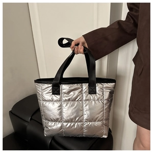 Détail d'un sac cabas argenté matelassé avec anse noire porté à la main au café