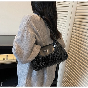 Détail du sac sous le bras en cuir noir embossé croco avec un nœud en métal argenté