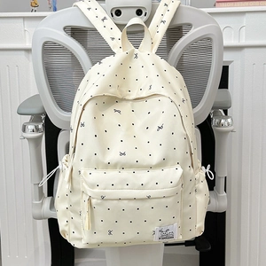 Sac à dos beige minimaliste à pois noirs et petits nœuds posé sur une chaise grise
