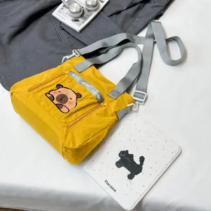 Detail showing the yellow nylon crossbody bag with a cute bear and multi-zipper pockets