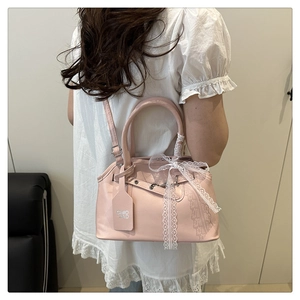 Détail du sac coque rose satiné avec un nœud en dentelle blanche et doubles anses