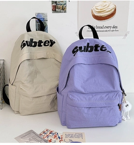 Dettaglio di zaini in nylon beige e viola con logo SubteX e decorazione in peluche