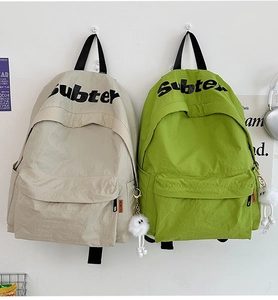 Dettaglio di zaini in nylon leggero beige e verde con ciondoli a sfera di peluche