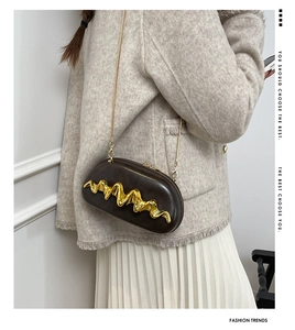 Macro shot of dark brown capsule bag featuring wave-shaped gold metal relief and chain