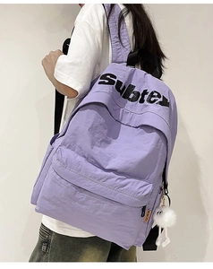 Dettaglio dello zaino in nylon viola chiaro con etichetta moda e ciondolo a pompon