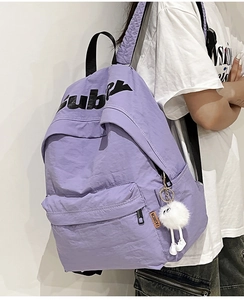 Vista laterale zaino in nylon viola con stampa a lettere e ciondolo di peluche bianco