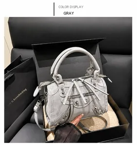 Detalle de bolso gris de ante con remaches plateados y borlas en caja de regalo