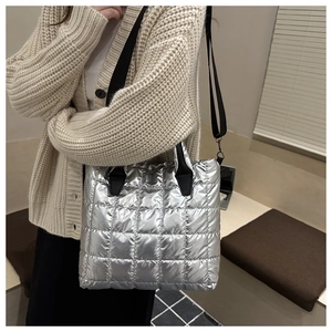 Détail du sac fourre-tout matelassé argenté avec bandoulière noire porté par un mannequin