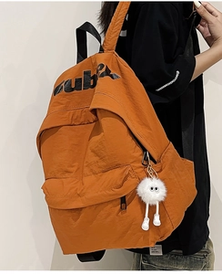 Dettaglio zaino in nylon arancione con stampa di lettere e ciondolo in peluche carino