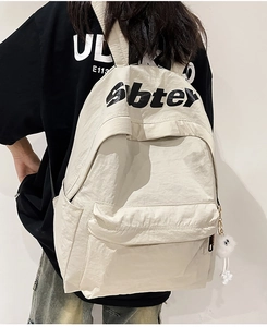 Dettaglio dello zaino in nylon bianco sporco con trama fine e scritte nere in alto