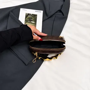 Detail der dunkelbraunen Minitasche mit gewelltem Goldgriff und schwarzem Innenfutter