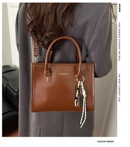 Détail du sac cabas marron brillant avec logo doré et breloques sur un manteau gris