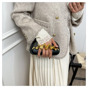 Detail der schwarzen Leder-Clutch mit gewelltem Goldgriff und eleganter goldener Kette