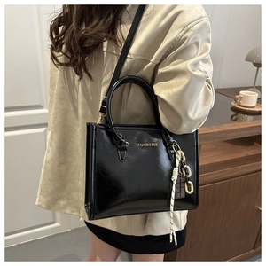 Detail of black glossy tote bag with gold lettering and decorative pendant charm