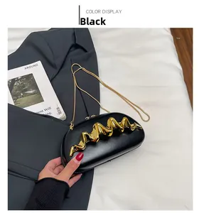 Detail of black acrylic clutch with golden fluid wave metal decor and chain strap