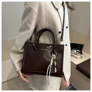 Détail du sac cabas en cuir verni marron brillant avec logo doré et chaîne décorative