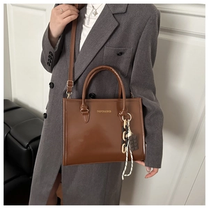 Détail d'un sac cabas marron en PU avec charms tendance et bandoulière sur costume gris