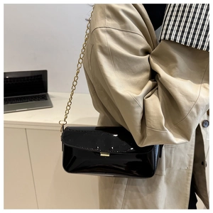 Fashionable black faux leather shoulder bag with gold chain strap on a female model