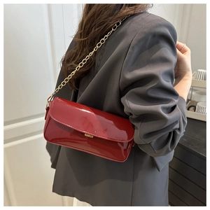 Detail of red patent leather baguette bag with gold chain strap on a grey blazer