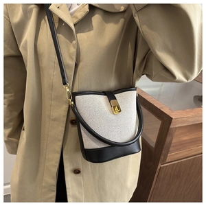 Canvas bucket bag detail showing contrast leather trim and gold twist lock clasp on model