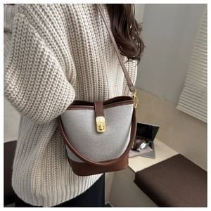 Close-up of canvas bucket bag with brown leather trim and golden metal swivel lock