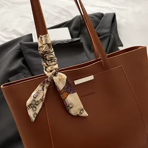 Détail d'un sac cabas marron avec foulard en soie et accessoire en métal sur fond gris