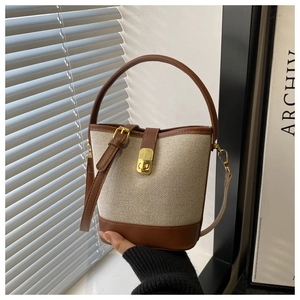 Detail of canvas bucket bag with brown leather trim, gold hardware and detachable strap
