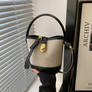 Minimalist beige canvas and black leather bucket bag with a golden lock closure