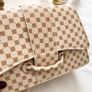 Detailopname van beige leer met bruin bloemmotief en gouden metalen beslag op de handtas